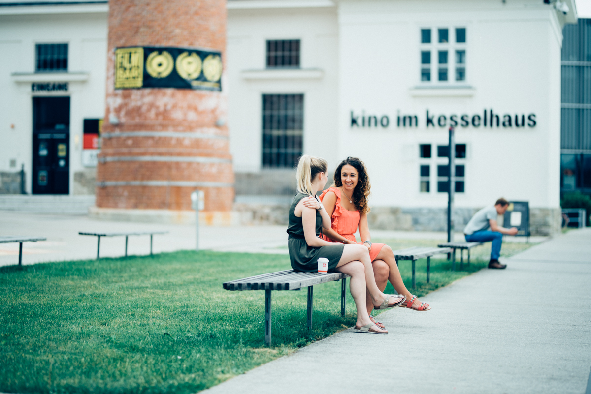 © Walter Skokanitsch Studierende sitzen auf Bänken auf der Campus Promenande vor dem Kino im Kesselhaus