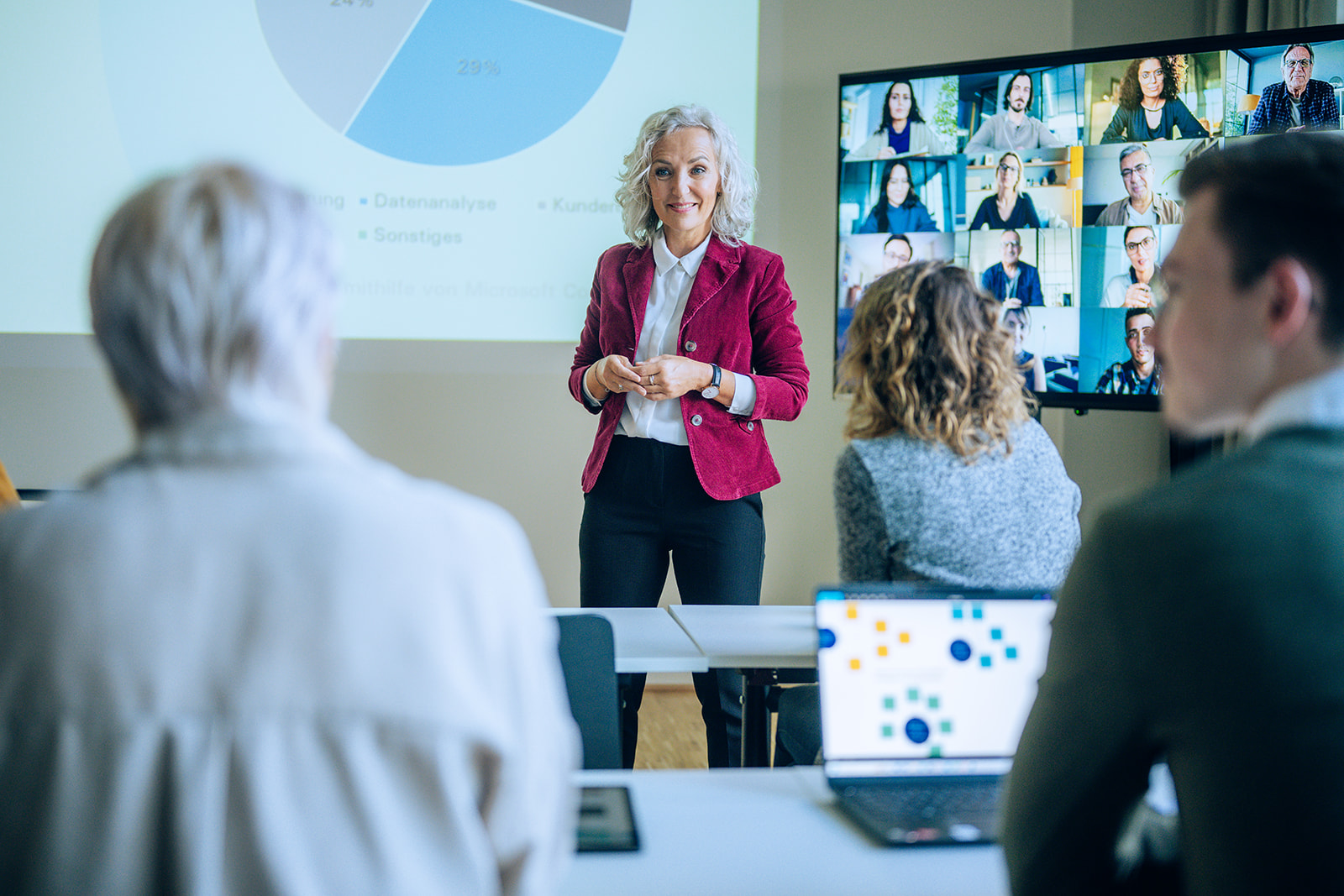Lecturer communicates with students in the context of a course. The lecturer is in focus. Students are connected both on site and online.