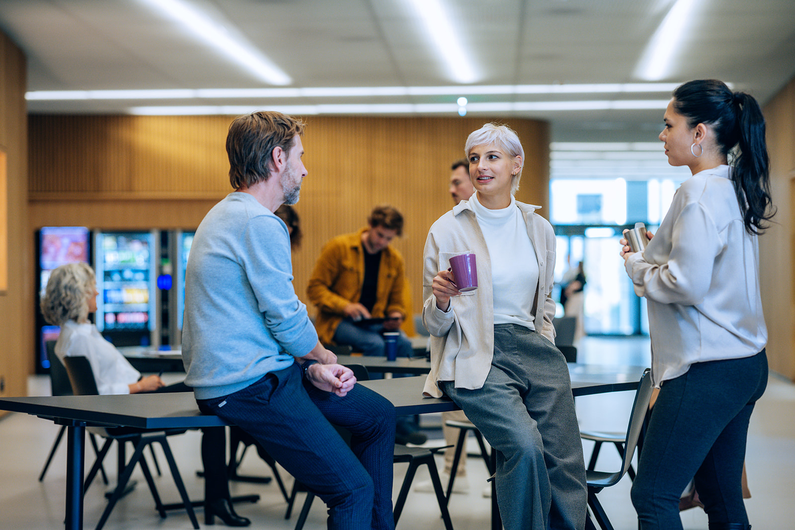 A group of students (two young women and a man in the foreground) talking during a break